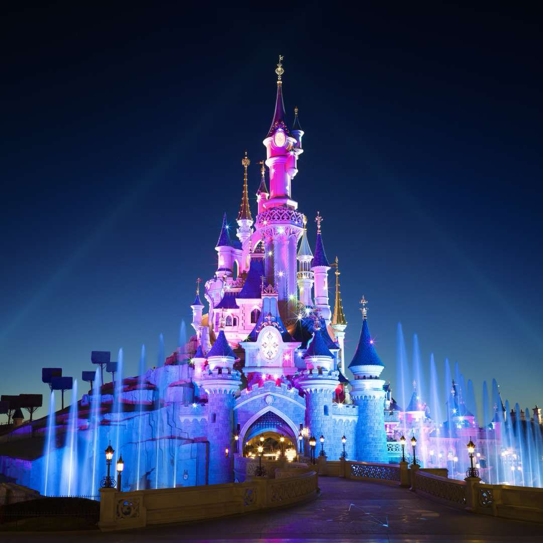 Illuminated Sleeping Beauty Castle at Disneyland Paris at night, representing luxury private transfers from Paris, CDG and Orly airports to Disneyland Paris.